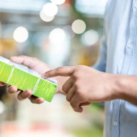 A man in a blue shirt is holding a green box and pointing at the details printed on it while shopping.