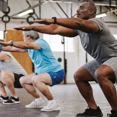 4 older men holding a squat in the gym