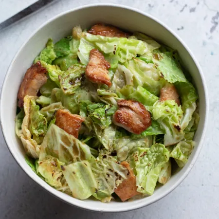 bowl filled with green cabbage and chicken stir fry on white counter