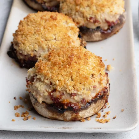 white plate with 2 stuffed Portobello mushrooms topped with breadcrumbs