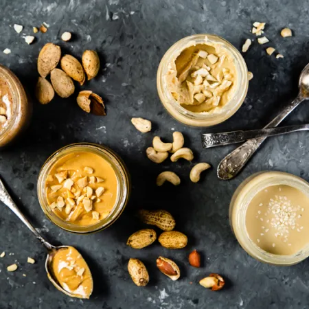 overhead shot of jars of different nut and seed butters with spoons on grey background
