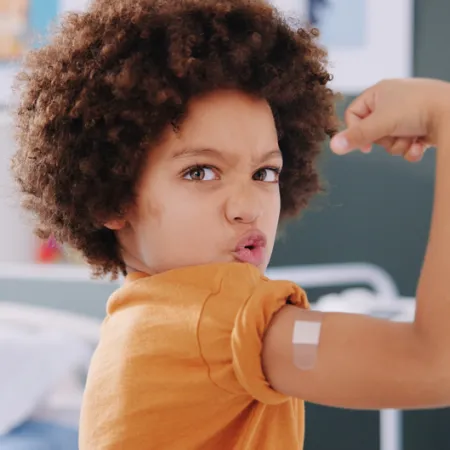 young child flexing muscles showing off a band-aid on their vaccine sight