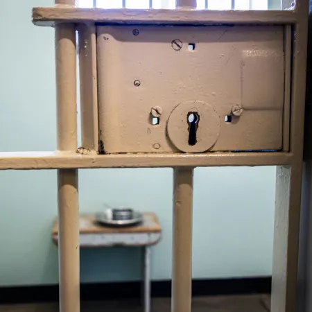 A locked prison cell with a metal food container inside.