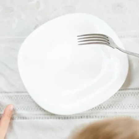 A child holds a fork over an empty plate