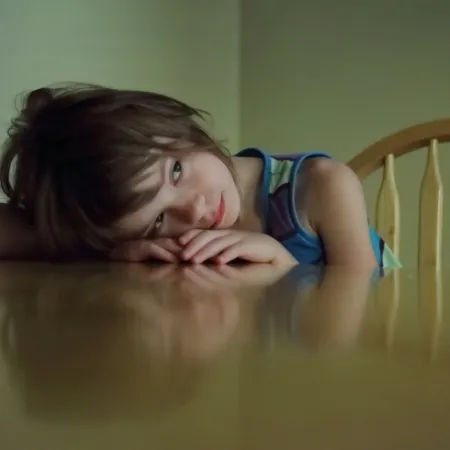 A little girl resting her head on an empty dining table. 