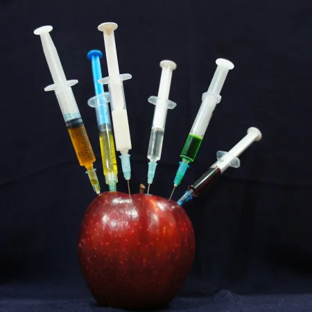 An apple with syringes sticking out of it.