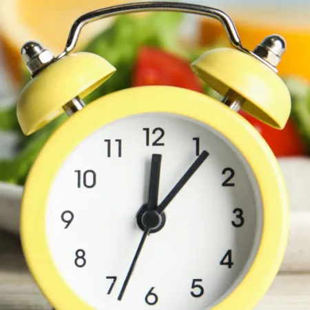 old yellow alarm clock in front of a plate of salad