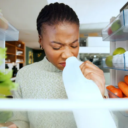 woman sniffing milk carton inside a fridge