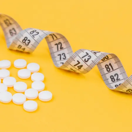 A measuring tape and weight loss pills on a yellow background