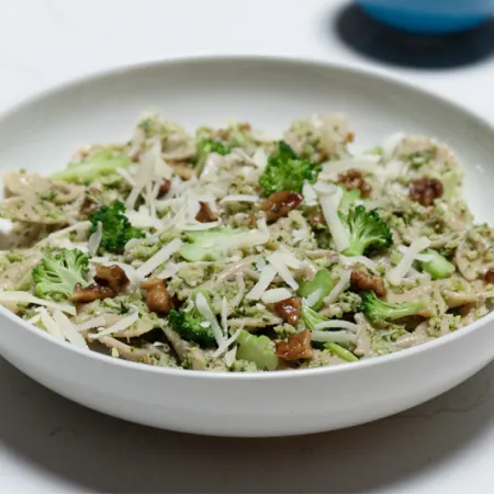 white bowl filled with pesto pasta and walnuts